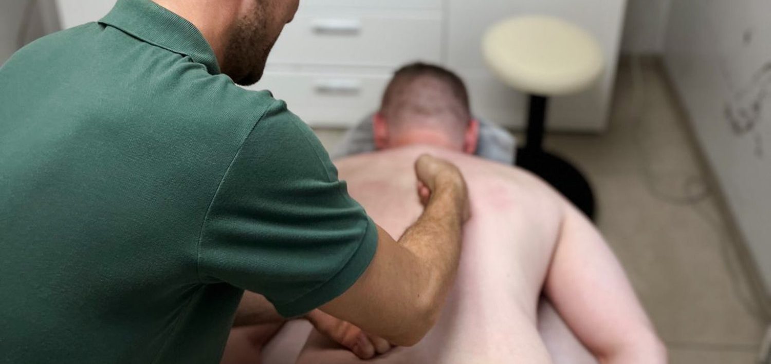 Masseur behandelt einen Klienten auf einer Liege in einem Behandlungsraum.
